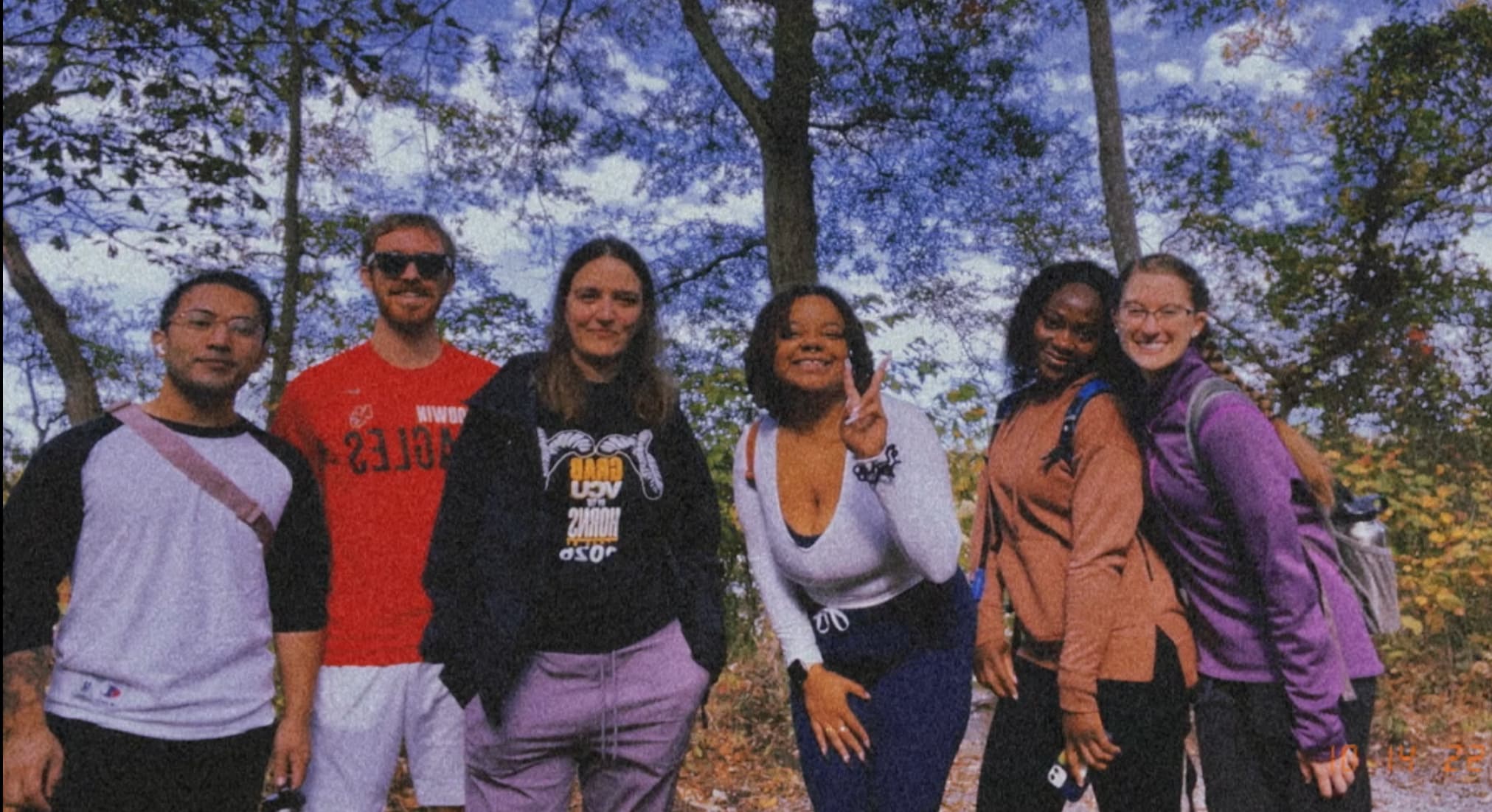 Six students posing in front of blue sky and trees